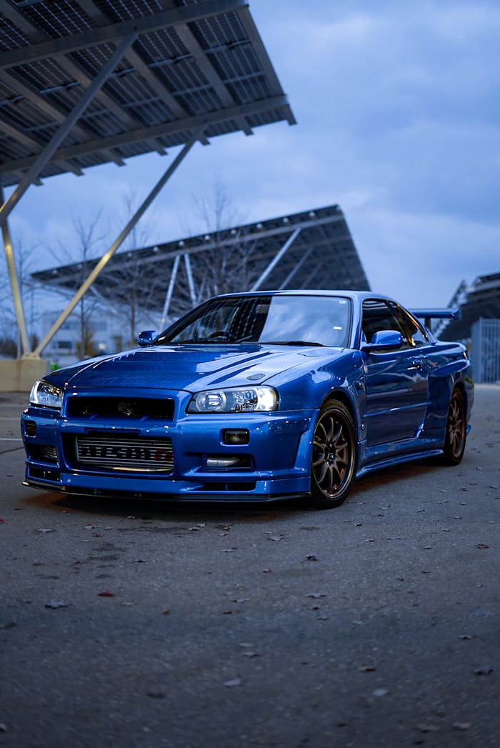 Blue sports car elegantly parked under solar panels at twilight.