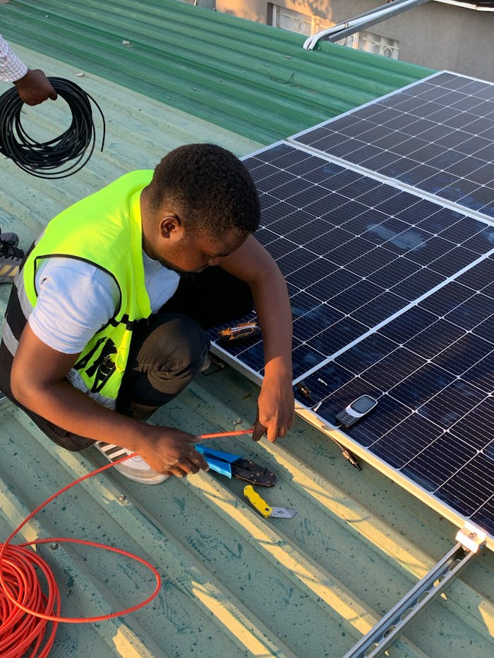 Technician working on solar panel installation with cables and tools on a sunny day.